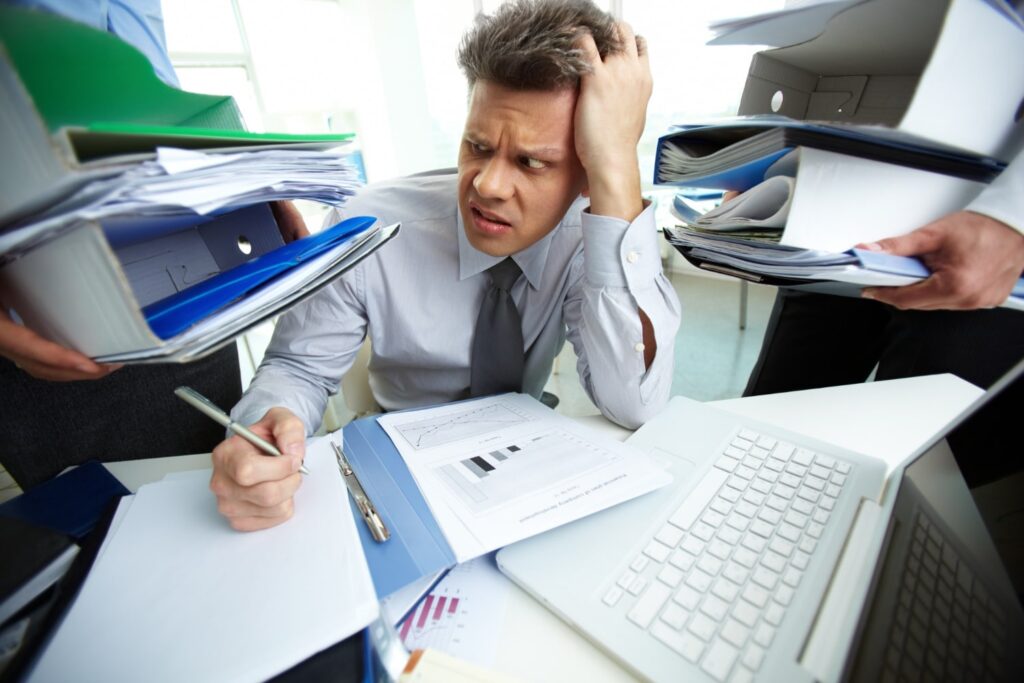Overwhelmed businessman surrounded by paperwork trying to do tax return
