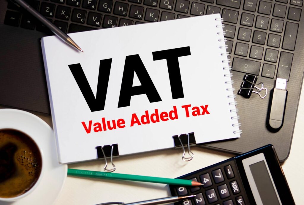 sticker with the word VAT on desk with calculator and laptop to calculate VAT return
